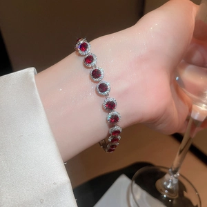 Gros plan d'un bracelet tennis en argent avec zircons rouges porté avec un verre à vin