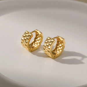 Polished 18K gold textured hoop earrings with embossed grid pattern on ceramic tray