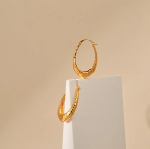 Close-up of hammered gold texture on oval irregular hoop earrings in 18K gold plated brass