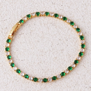 Detail van een gouden tennisarmband ingelegd met groene en witte zirkonia steentjes