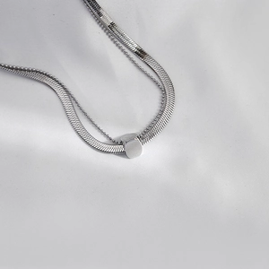 Detail of layered silver snake chain necklace with rectangular pendant on white fabric