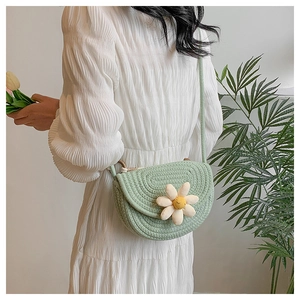 Detail of green woven saddle bag featuring a 3D white flower charm and slim strap