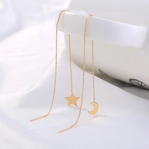Detail of gold star and crescent moon tassel earrings hanging on white ceramic cup