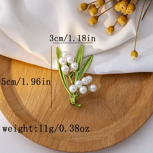 Detail view of leaf brooch with green enamel and white pearl on wood tray with measurements