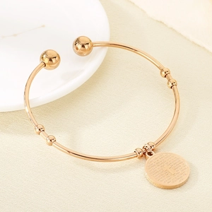 Detail of rose gold open bracelet featuring a round charm with Spanish Lord's Prayer engraving