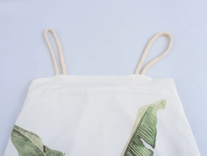 Detail view of woven rope shoulder straps and green palm leaf print on a white summer dress