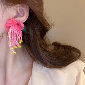 Close-up of pink fabric flower earrings with beaded tassels worn by a model
