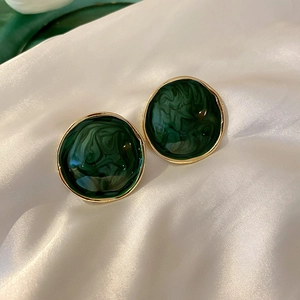 Macro shot of dark green enamel geometric earrings with gold trim on white silk