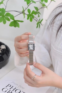 Close-up of rectangular silver watch with stainless steel band and roman numerals