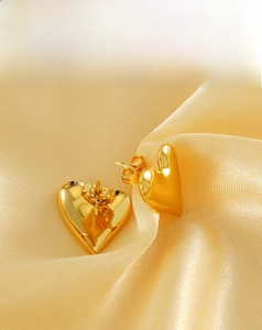 Close-up of golden 18K heart-shaped stud earrings on champagne satin fabric
