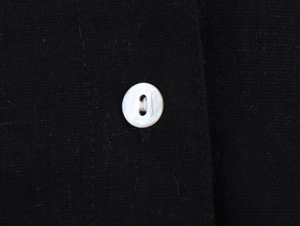 Close-up of white pearlescent button on black linen fabric showing texture and detail