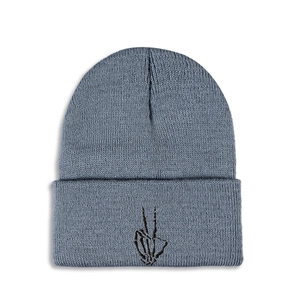 Detail of blue knitted beanie featuring a black embroidered skull gesture on the front cuff
