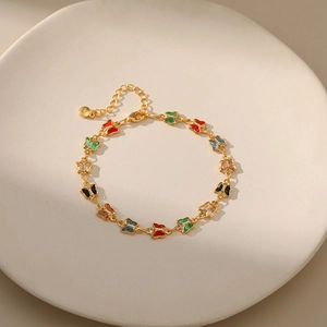 Close-up of gold-plated butterfly bracelet with colorful enamel charms on ceramic tray