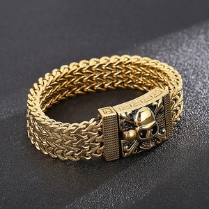 Detailed close-up of gold skull link bracelet with intricate woven texture on dark background