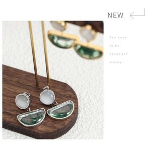 Detailed view of silver-tone earrings with white cat eye stone and green resin charms
