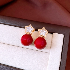 Macro shot of star-shaped gold earrings with red pearls in a beige velvet jewelry box
