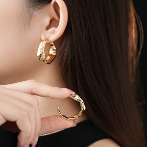 Detailed close-up of C-shaped golden earrings with organic crumpled texture