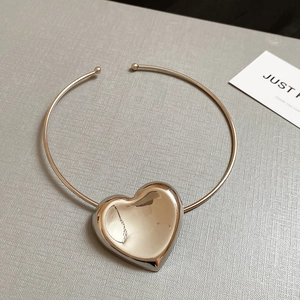 Macro shot of silver heart pendant on gold metal choker with polished finish