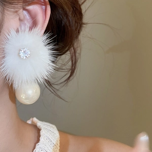Close-up of elegant earring featuring white fur pompom, zircon stud and pearl detail
