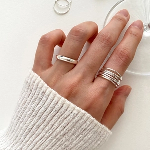 Detail shot of multi-layered silver geometric rings on a model hand with clear glassware