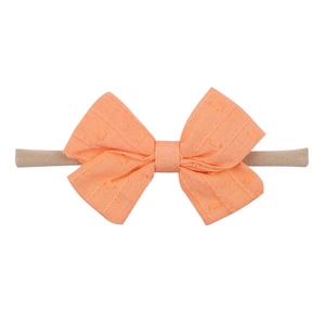 Detailed view of coral orange baby headband with Swiss dot texture bow and nylon band