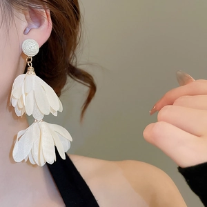 Detailed view of model wearing white layered chiffon flower earrings with raffia tassels