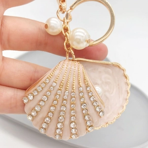Detail of a pink seashell keychain featuring rhinestones, gold edges, and white pearls