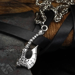 Detailed close-up of a silver Viking axe pendant on textured metal and leather background