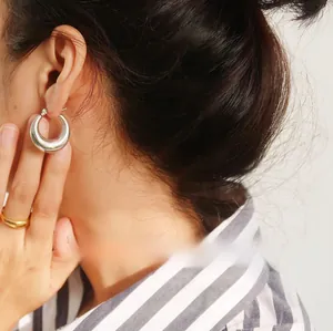 Macro detail of polished silver hoop earrings and gold ring on a model with minimalist style