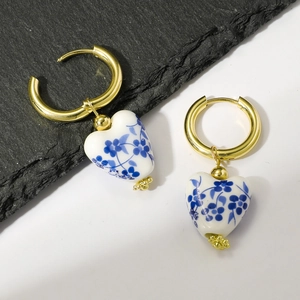 Macro view of golden hoops with blue and white heart porcelain pendants on stone