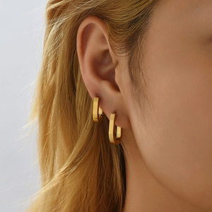 Detail of 18K gold-plated oval hoop earrings worn on ear lobe and cartilage