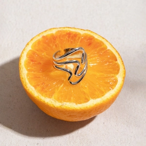 Silver wavy stainless steel ring placed on a fresh orange showing detailed metal texture