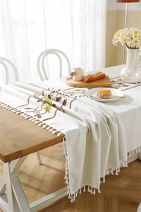 Detail of embroidered floral patterns and tassels on a cream cotton linen table runner