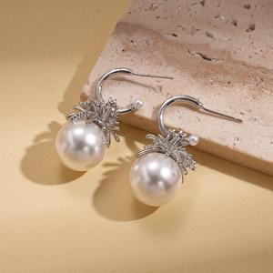 Detail of elegant C-shaped pearl earrings with silver leaf metal work on textured stone