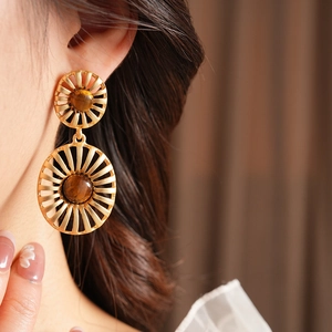 Close-up of vintage gold sunburst earrings with tiger eye stone on model's ear