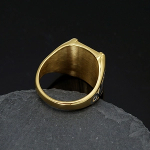 Macro view of men's gold stainless steel eagle ring on a dark textured stone background