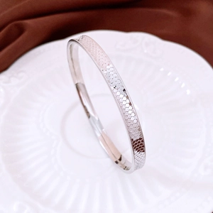Close-up of silver-tone metal bracelet featuring geometric textured pattern on white ceramic