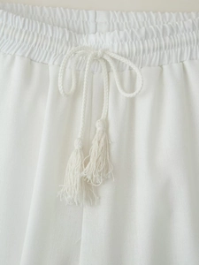 Detail of white cotton linen trousers with elastic waist and tasseled drawstring cord