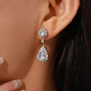 Close-up of teardrop zircon earrings with halo stones worn by a model in silver finish