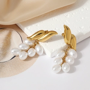 Detailed shot of gold-plated wing earrings with clustered pearl tassel on silk background