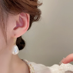 Close-up of elegant gold hook earring with large white teardrop pearl on female model