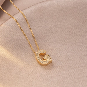 Close-up of golden initial letter G pendant with zircon stones on champagne satin fabric