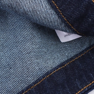 Gros plan du tissu denim bleu foncé avec des coutures orange et une texture de qualité