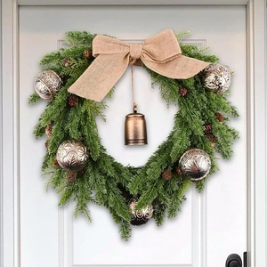 Christmas wreath with green pine needles, silver textured balls and rustic bell on white door