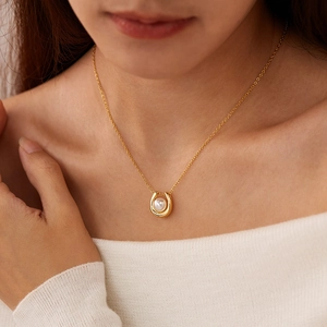 Close-up of horseshoe pendant necklace with white pearl on elegant gold chain