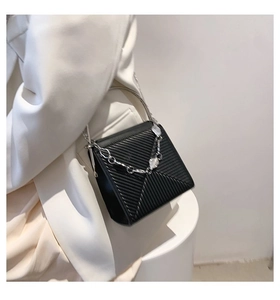 Close-up of black handbag featuring twill texture, metal handle, and thick silver chain