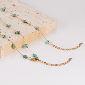 Luxurious gold chain necklace with natural turquoise stones on beige stone background
