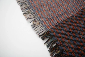 Macro view of wool blend scarf featuring orange and blue herringbone weave and fringe detail