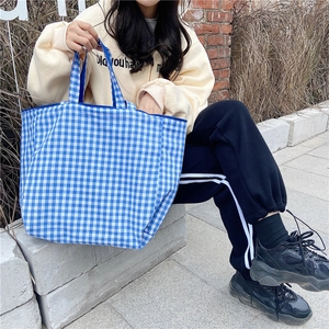 Detailed outdoor shot of a large blue checkered canvas tote bag worn by a model