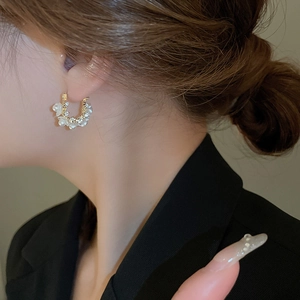 Close-up of gold hoop earring with white floral detail and micro-pave zircons on model